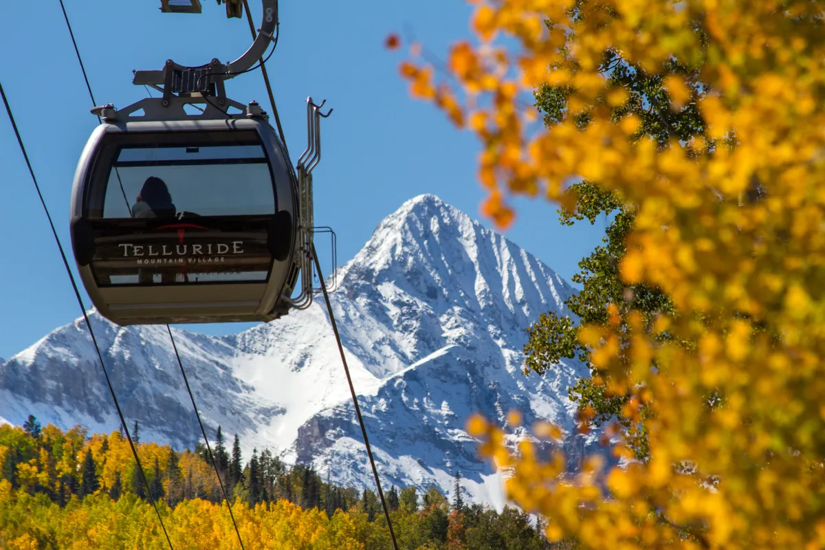 This image highlights a gondola ascending against a backdrop of snow-capped mountains and vibrant autumn foliage. The scene captures the essence of Telluride’s unique lift-access lifestyle, with both the gondola and surrounding landscape signaling year-round adventure. The mood is both adventurous and peaceful, emphasizing the thrill and tranquility of exploring the outdoors.