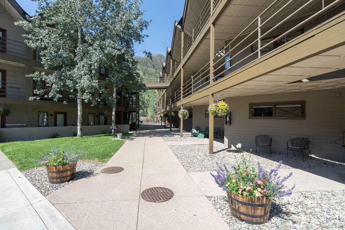 A welcoming outdoor pathway flanked by flower pots and low-rise buildings, evoking a cozy, walkable atmosphere. The scene suggests leisurely strolls, friendly interactions, and the convenience of a pedestrian-friendly area with immediate access to outdoor relaxation and social spaces.