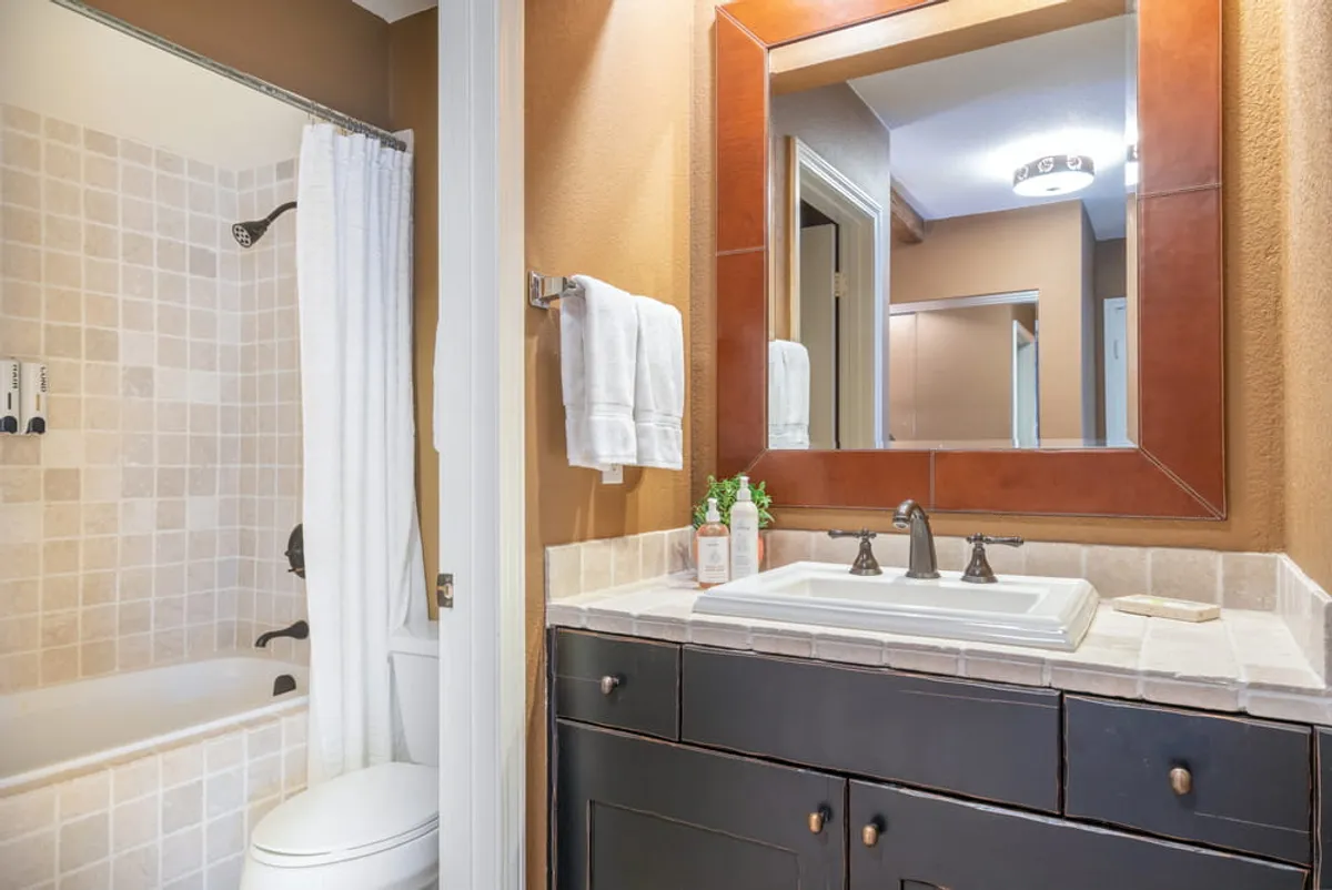 A clean, bright bathroom featuring a large mirror above a modern sink, a towel rack displaying plush white towels, and a bathtub with gleaming fixtures. The room exudes a sense of freshness, comfort, and practical convenience.
