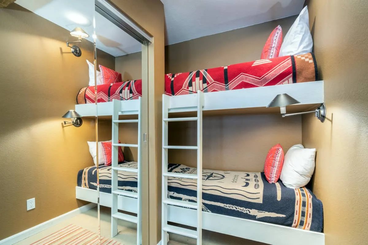 A close-up of the bunk beds with cheerful, colorful bedding, set in a hallway nook with a mirror, creating a playful and inviting atmosphere. This reinforces the section's emphasis on family-friendly sleeping arrangements and the sense of adventure for kids.