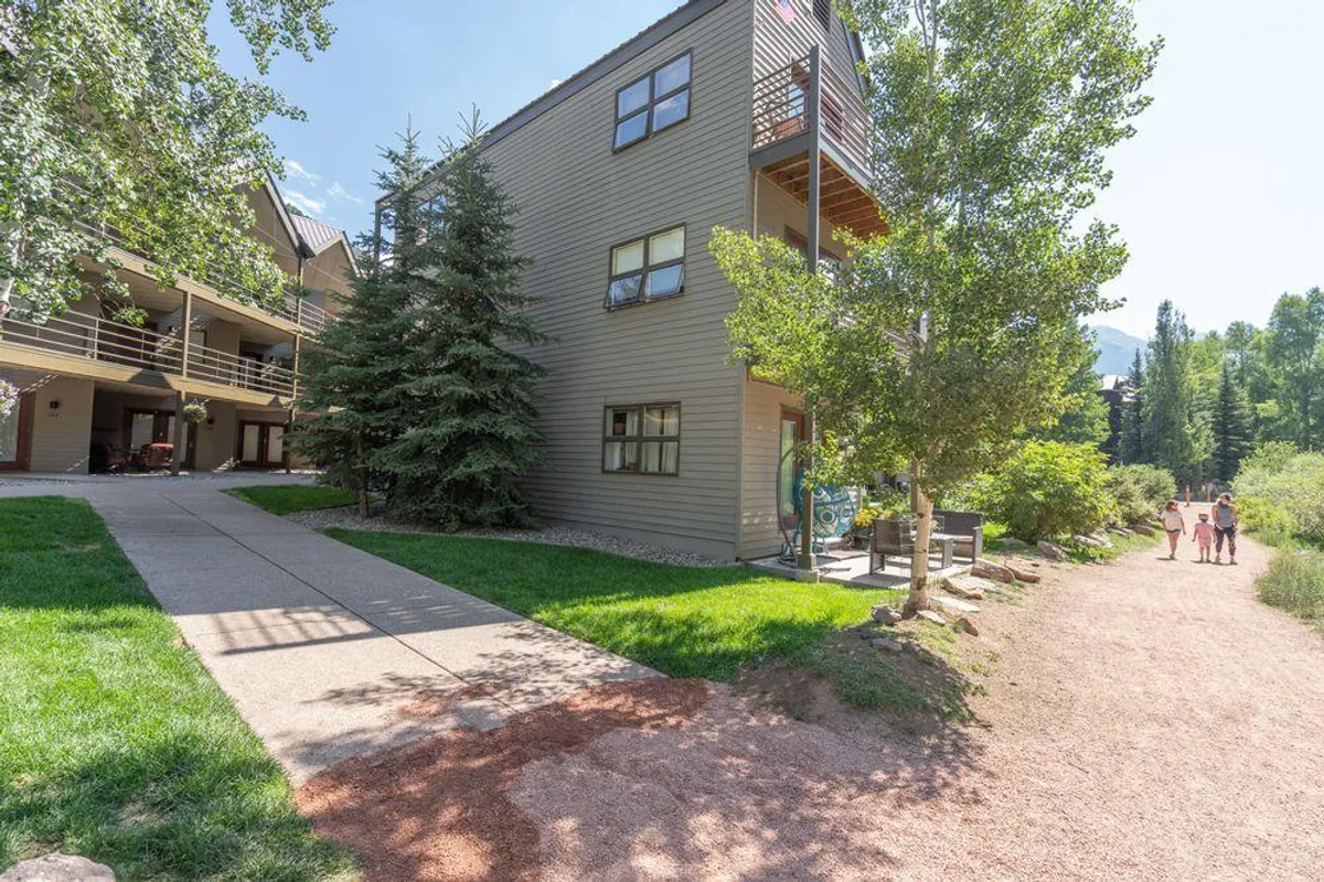 This exterior shot displays a building surrounded by tall trees, with a pathway leading up to it and a balcony overlooking the natural surroundings. The scene is tranquil and suggests the ease of stepping outside to enjoy nature, walk, or relax on the balcony.
