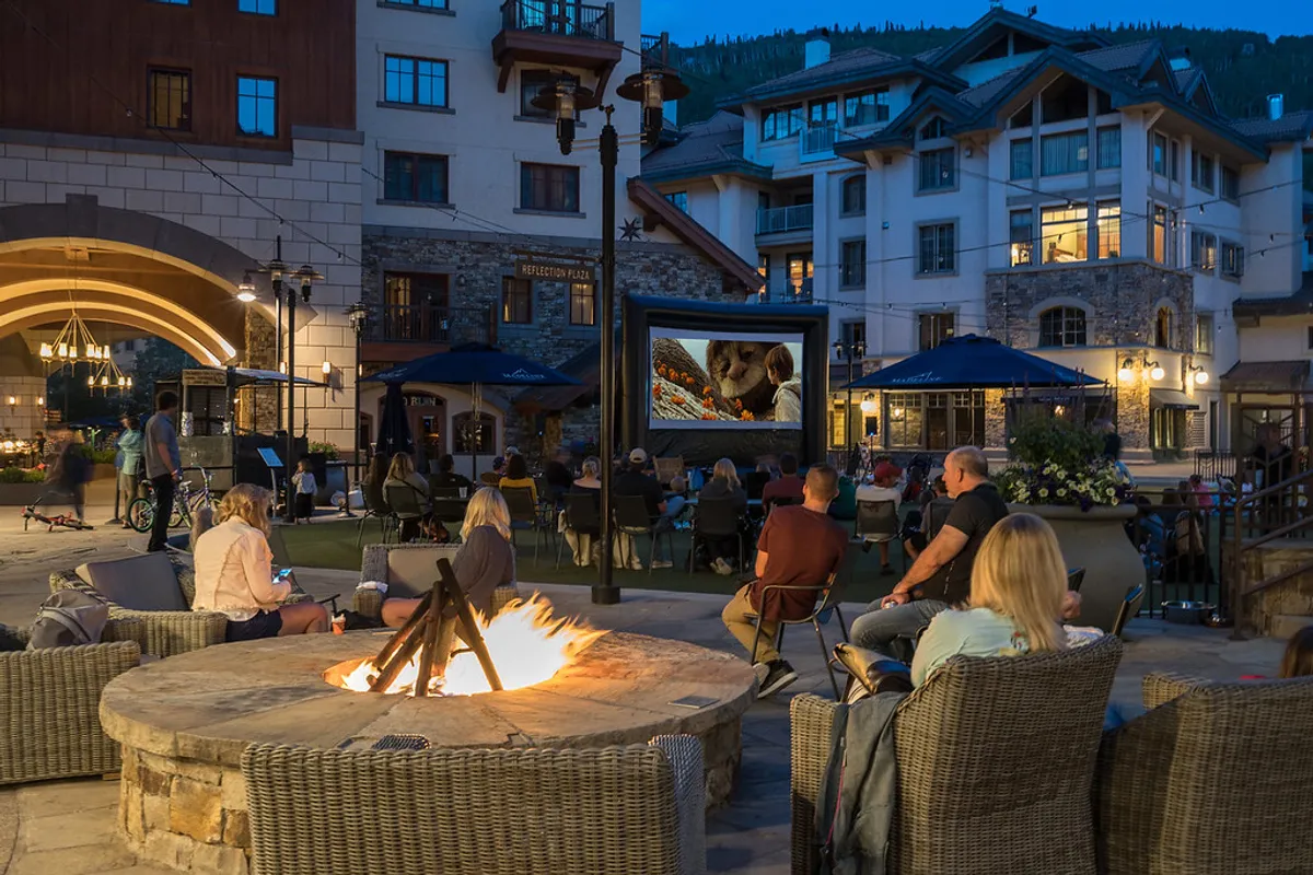A communal outdoor setting with a fire pit, cozy seating, and an outdoor movie screen, suggesting social gatherings under the stars. The atmosphere is warm and inviting, ideal for shared evenings and memorable moments beyond the confines of the home.
