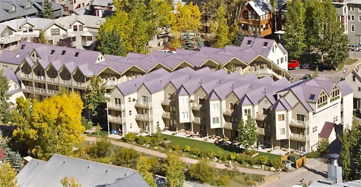 Rows of charming townhouses are set amid lush summer greenery, with inviting walking paths winding through the landscaped community. The scene radiates warmth and a sense of communal outdoor living, ideal for family strolls and gatherings.